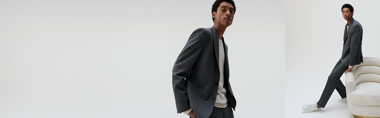 A model wearing a heather-grey suit with an ivory crewneck sweater.