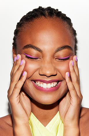A smiling woman with pink eyeliner and a fresh manicure.